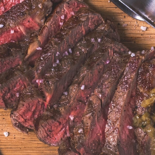 Close-up of sliced medium-rare steak with coarse salt and pepper on a wooden board.