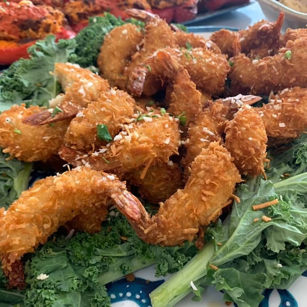 Close-up of golden-brown coconut shrimp, garnished with parsley and shredded coconut, on a bed of kale.