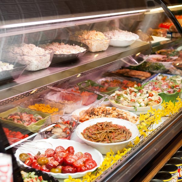 A deli display case filled with various salads, including pasta, potato, and green bean dishes.