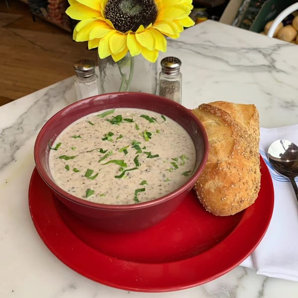 Creamy mushroom soup in a red bowl with a side of crusty bread on a marble table.