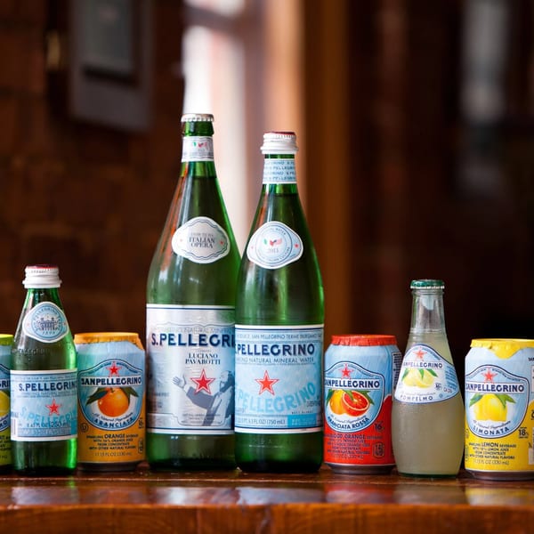 A collection of San Pellegrino sparkling water bottles and cans in various flavors on a wooden surface.