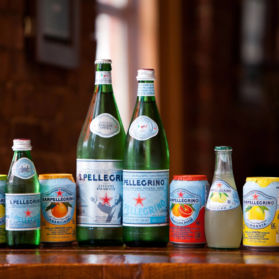 A collection of San Pellegrino sparkling water bottles and cans in various flavors on a wooden surface.