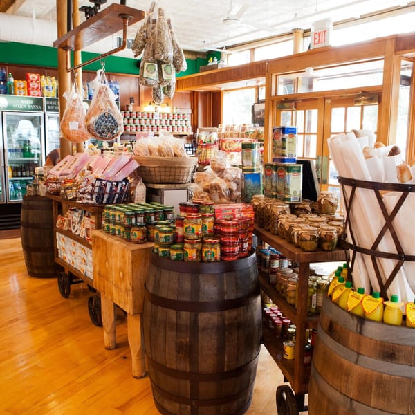 An Italian deli interior with hanging cured meats, barrels, and shelves filled with various food products.