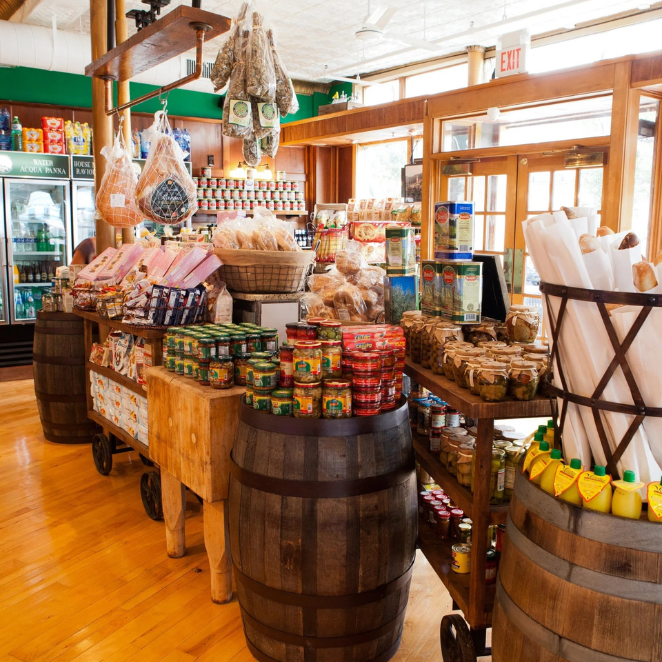 An Italian deli interior with hanging cured meats, barrels, and shelves filled with various food products.