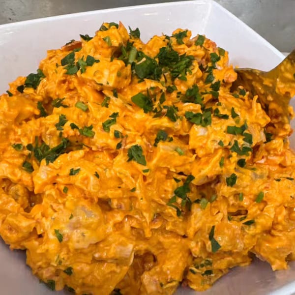 Close-up of a creamy orange chicken salad with green herbs in a white bowl, with a spoon.