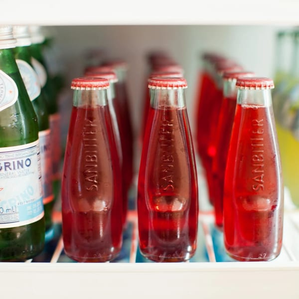 Sanbitter and San Pellegrino bottles with red and green liquids in a refrigerator.