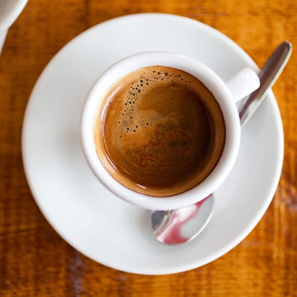 Close-up of a white cup of espresso with crema, on a matching saucer with a spoon.