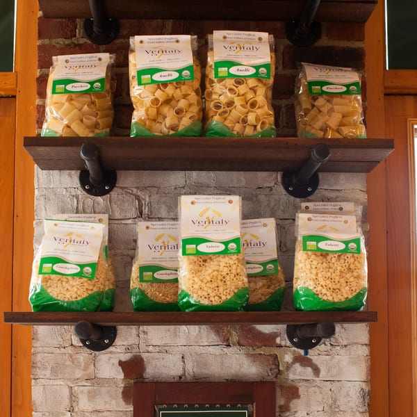 Bags of Veritaly brand organic pasta, including paccheri, anelli, conchigliette, and tubetti, on wooden shelves.