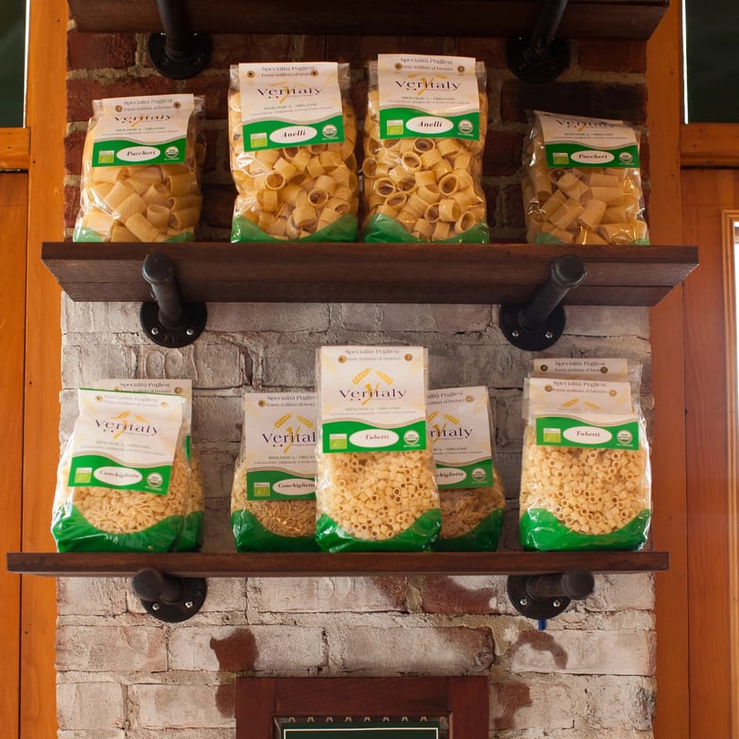 Bags of Veritaly brand organic pasta, including paccheri, anelli, conchigliette, and tubetti, on wooden shelves.