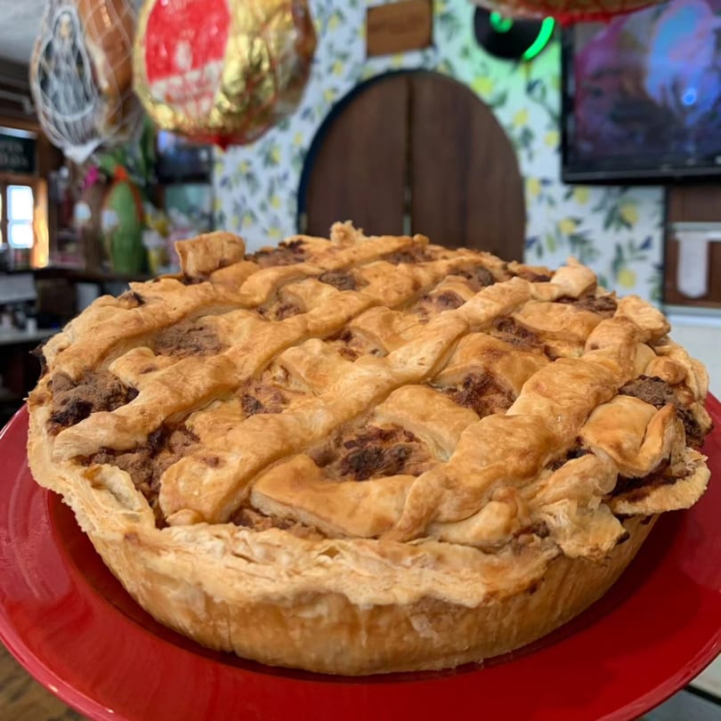 A golden-brown lattice-top pie with a rich, dark filling, served on a vibrant red plate.