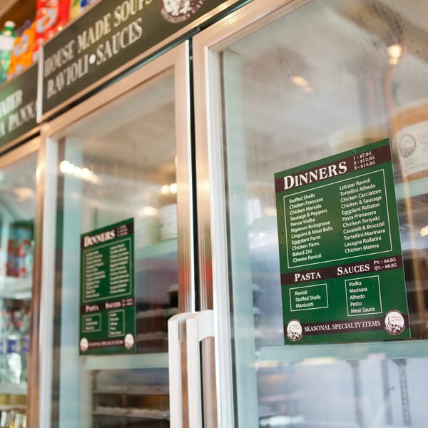 A deli display case with a menu of Italian dinners, pasta, and sauces on the glass.