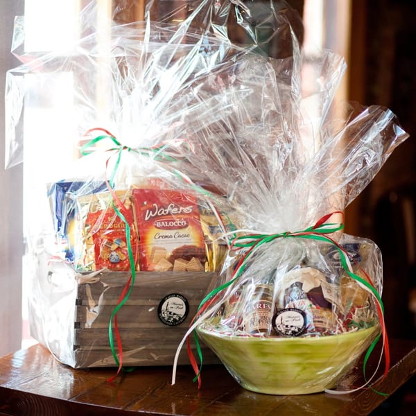 Two gift baskets filled with Italian market products, wrapped in cellophane and tied with red, white, and green ribbons.