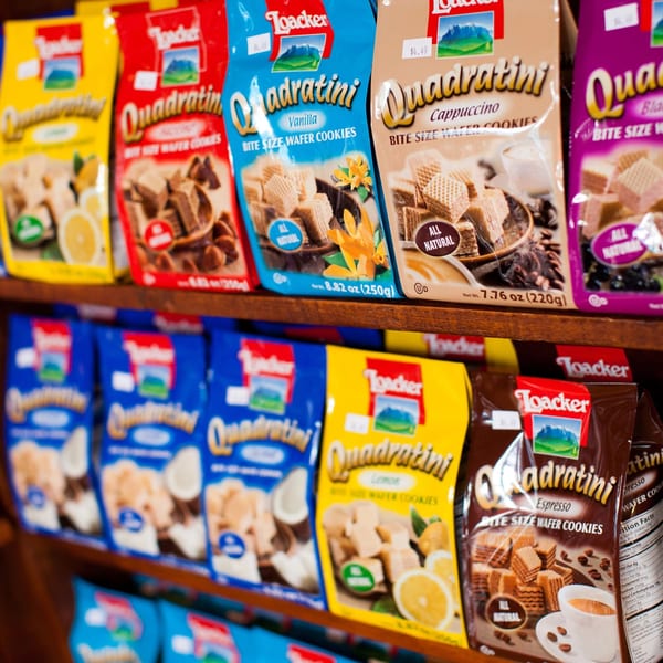Rows of colorful Loacker Quadratini wafer cookie bags in various flavors on a wooden shelf.
