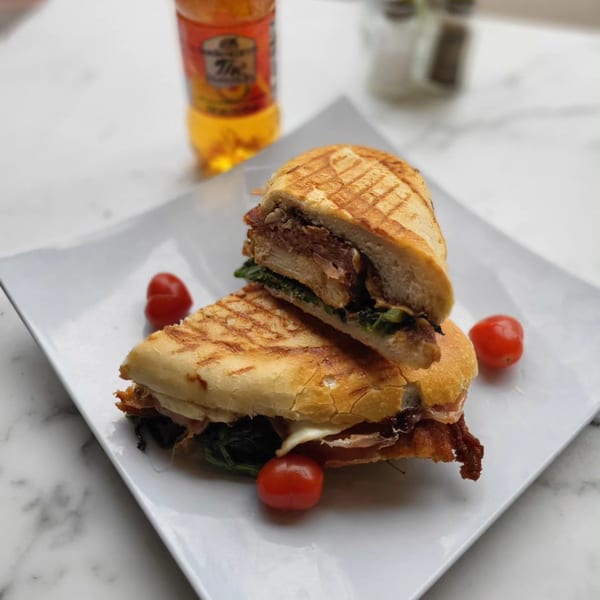 Grilled panini sandwich, cut in half, with cherry tomatoes on a white plate, and a drink in the background.