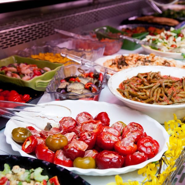 A buffet spread with various dishes, including stuffed red peppers, green beans, and salads.
