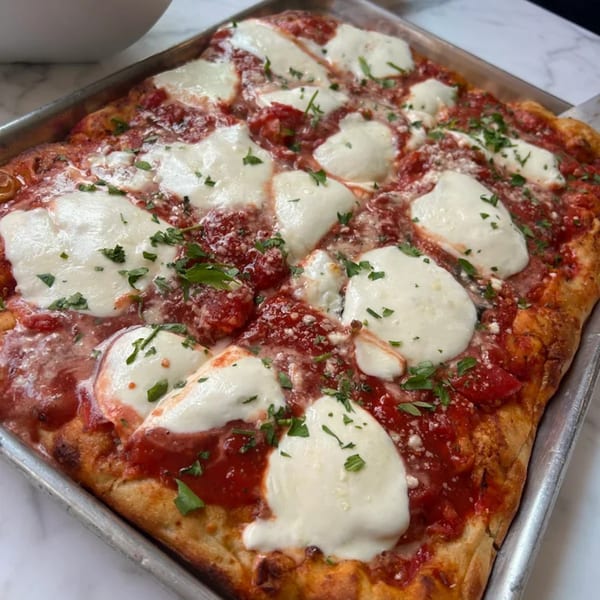 Square Detroit-style pizza with melted mozzarella, red sauce, and fresh parsley in a metal pan.