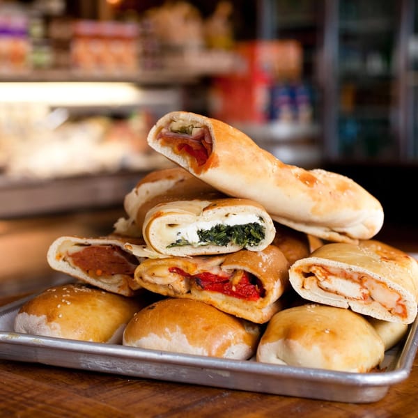 A metal tray filled with various strombolis, some sliced open to reveal fillings like pepperoni, spinach, and chicken.