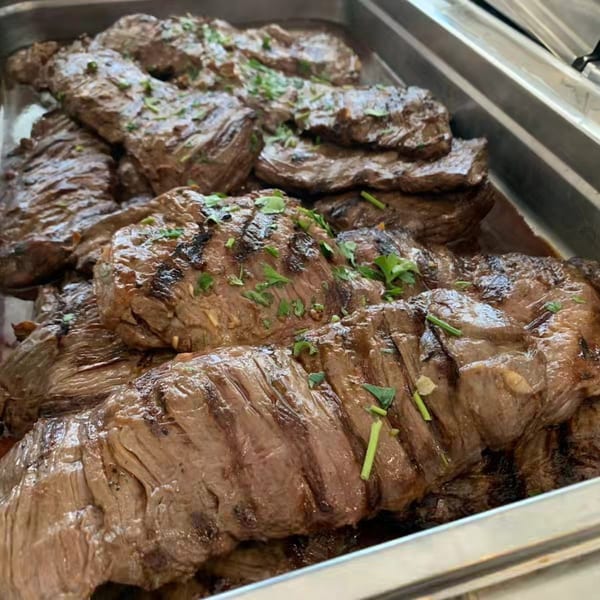 Close-up of grilled steak slices garnished with fresh herbs in a metal serving tray.