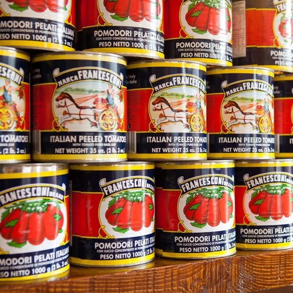Francesconi Italian peeled tomato cans stacked on a wooden shelf, featuring a horse-drawn cart logo.