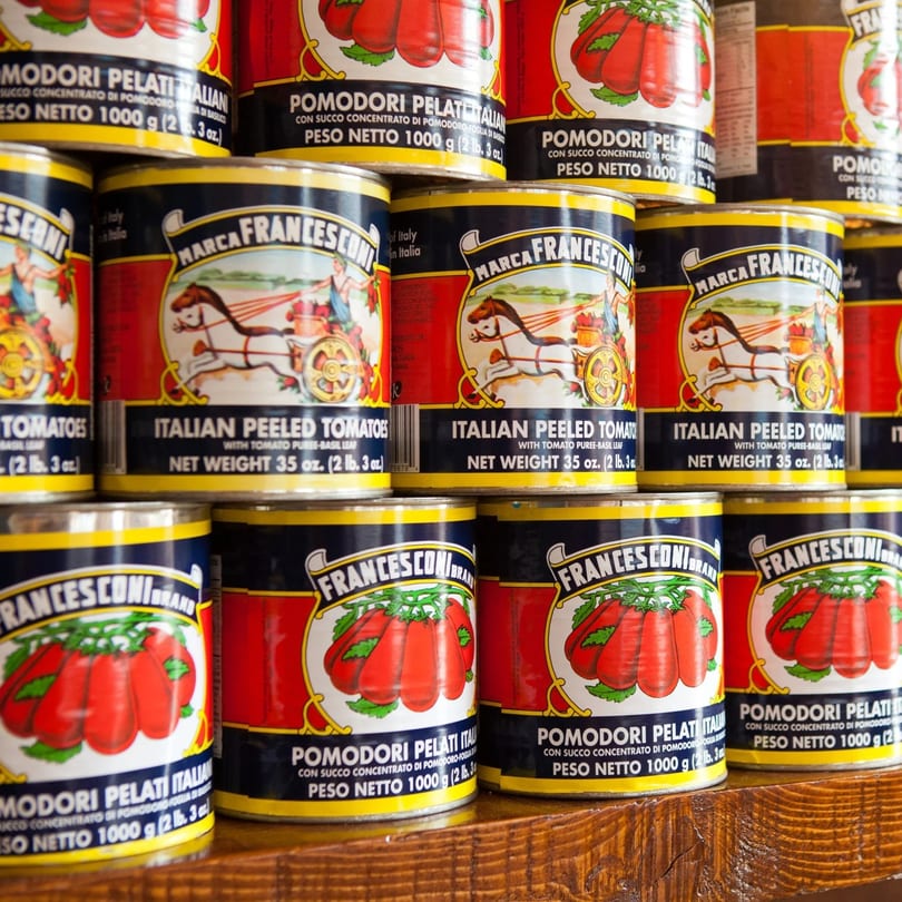 Francesconi Italian peeled tomato cans stacked on a wooden shelf, featuring a horse-drawn cart logo.