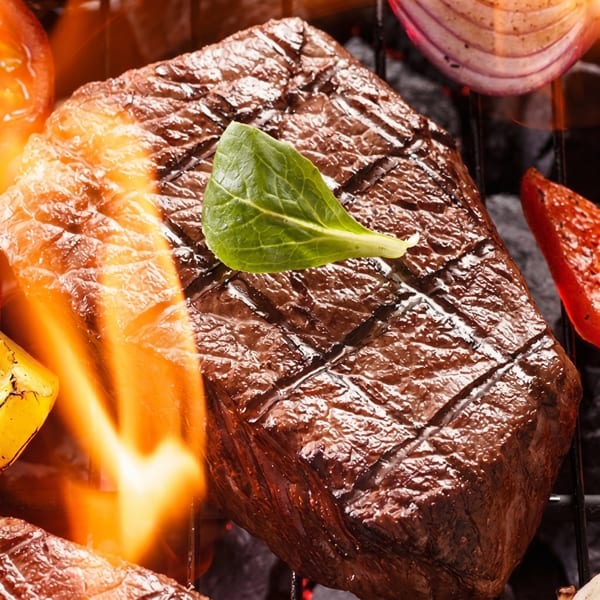 Grilled steak with grill marks and a green herb, surrounded by flames and vegetables.