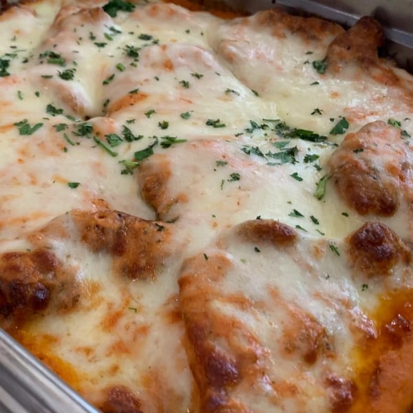 Close-up of baked pasta with melted mozzarella cheese and parsley in a metal pan.