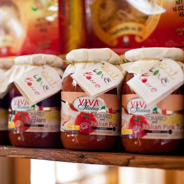 Three jars of Viva Italia tomato sauce, two "Italian Pink" and one "Eggplant", on a wooden shelf.