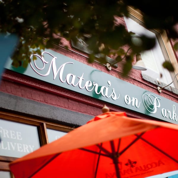 The Matera's on Park restaurant sign in white script lettering above a bright orange umbrella.