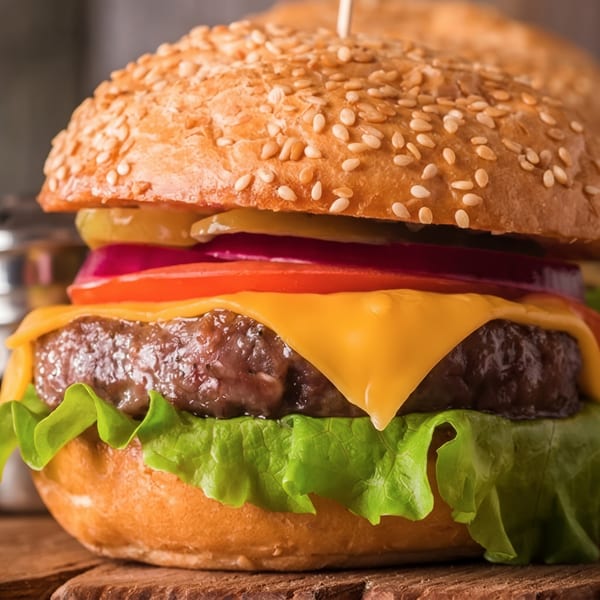 Close-up of a cheeseburger with lettuce, tomato, onion, pickles, and a sesame seed bun.
