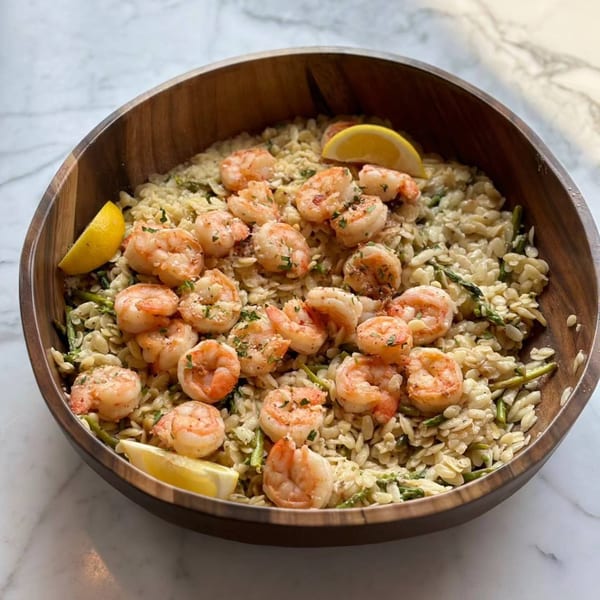 Shrimp and orzo pasta with asparagus and lemon wedges in a wooden bowl on a marble surface.