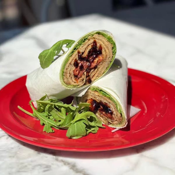 Two halves of a wrap with meat, sauce, and lettuce, served on a red plate with arugula.