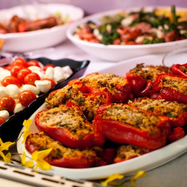Platter of red bell peppers stuffed with rice and meat, alongside cherry tomatoes and mozzarella balls.