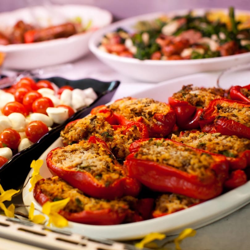 Platter of red bell peppers stuffed with rice and meat, alongside cherry tomatoes and mozzarella balls.