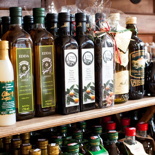 Bottles of olive oil and balsamic vinegar line wooden shelves in a specialty food store.
